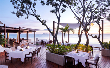 Beach Club dining area at Amanpulo with wooden deck, white-clothed tables and views towards the Philippine sea at dusk.