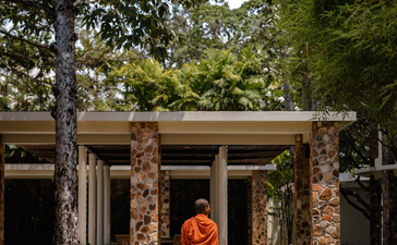 Buddhist monk in saffron robes walking through a stone pavilion at Amansara, Cambodia.