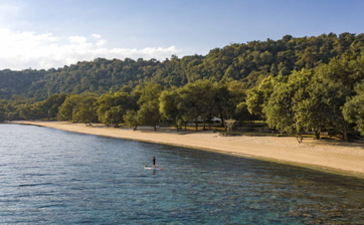 安缦湾澜度假村的沙滩，清澈蓝水与金色沙滩相接，背景为茂密树林。