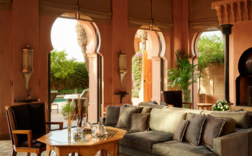 阿玛珍纳度假村Al Hamra套房客厅，配有摩洛哥拱形门窗、灰色沙发和传统木制家具。