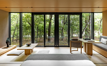 Spacious bedroom at Aman Kyoto with floor-to-ceiling windows overlooking forest, minimalist furnishings and natural light.