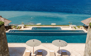 Piscina infinita con vistas al mar en Amankila resort, Bali, con tumbonas y sombrillas.