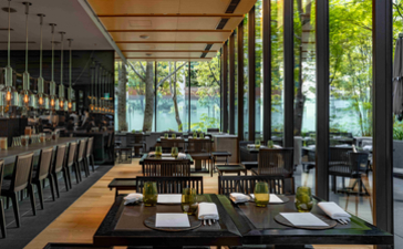 Dining venue at Aman Tokyo with floor-to-ceiling windows overlooking spring foliage, wooden ceiling beams, and dark furnishings.