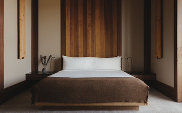 Amangani Suite principal bedroom with wooden bed frame and white pillows, framed by warm timber panelling.