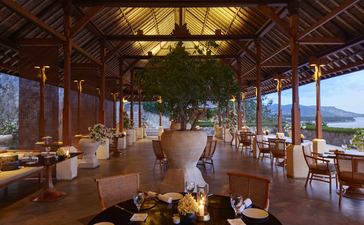 Amankila restaurant interior with wooden beamed ceiling, dining tables, and mountain views through open sides.