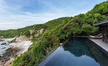 Swimming pool overlooking the coastline at Amanoi, with lush hillside and calm waters below.