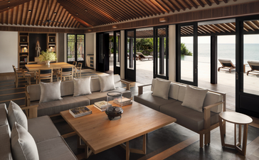 アマノイ リゾートの広々としたスイートの居間。木製の天井、グレーのソファ、木製テーブル、大きな窓から自然光が差し込む。