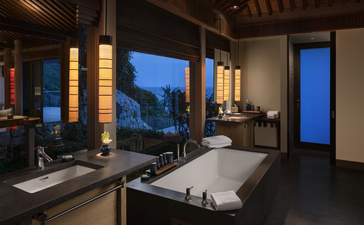 アマノイ リゾートのバスルーム。夜間、窓から景色を望む浴槽と洗面台。