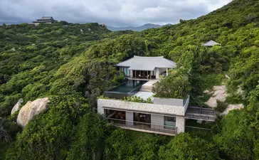 Amanoi residence with modern architecture set among lush green hillside vegetation in Vietnam.