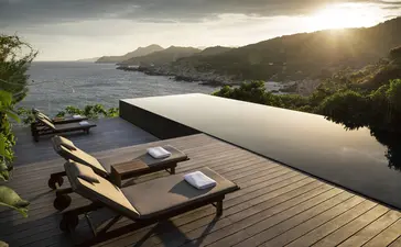 Wooden sun lounger on a terrace overlooking an infinity pool and coastal landscape at Amanoi.