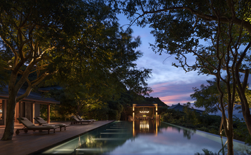 アマノイ リゾートの静かなプールが夕暮れ時に灯りに照らされ、周囲の樹々が映り込んでいる。