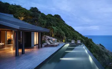 Swimming pool overlooking the sea at Amanoi, with illuminated pavilion nestled into the hillside at dusk.
