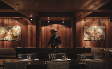 Warm-lit dining room at Amangani with artwork displayed on terracotta-coloured walls and table settings below.