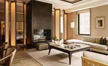 Corner Suite living room at Aman New York with dark wood paneling, cream furnishings, and floor-to-ceiling windows.