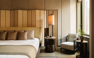 アマン ニューヨークのコーナースイートの寝室。木製パネルのヘッドボードと大きな窓が特徴。