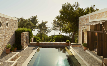 Amanruya pavilion with rectangular plunge pool overlooking partial sea view, framed by stone walls and pine trees.