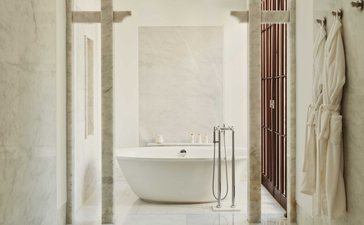 Amanruya bath pavilion with freestanding white bathtub and neutral stone finishes.