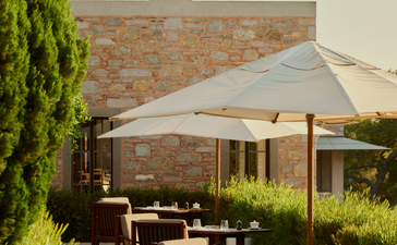 Poolside dining terrace at Amanruya with stone architecture, shaded seating and verdant landscaping.