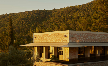 Amanruya's main pool and Ottoman lounge overlooking calm water at golden hour, surrounded by forested hillside.