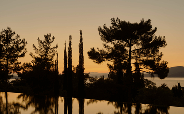 Silhouetted cypress and pine trees reflected in still water at Amanruya at sunset.