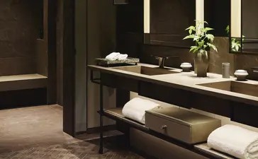 حمام Corner Suite في أمَان نِيُويُورك، مع حوض غسيل أنيق وإضاءة دافئة.