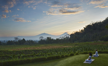 Guest practising yoga on a grass lawn at Amanjiwo, with volcanic peaks visible across the valley at dawn.