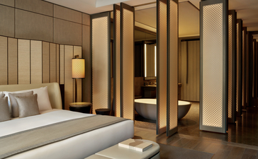 安缦纽约酒店套房卧室，配有米色床铺、木质屏风隔断和温暖照明。