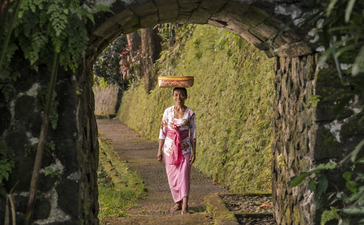 Woman in pink sarong walking through stone archway covered in moss at Amandari, Bali.