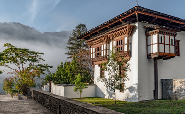 Traditional Bhutanese farmhouse at Amankora with painted wooden details and morning mist in the valley beyond.