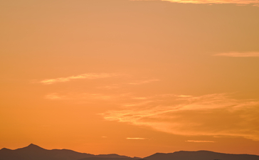 Sunset over calm waters with mountains silhouetted against an amber sky at Amanruya.