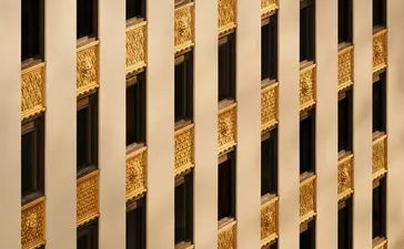 Detalle arquitectónico de la fachada del edificio Crown en Aman New York, con patrón de franjas verticales doradas y negras.
