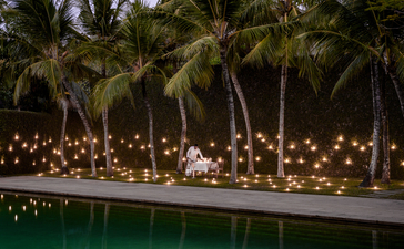 Candlelit outdoor dining setup along a water feature at Amangalla, lined with palm trees at dusk.