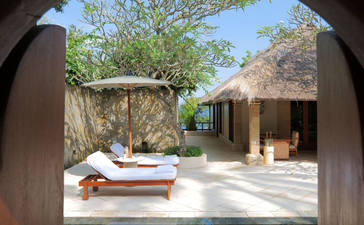 Pool Suite at Amankila resort in Indonesia, framed through curved stone archway with sunbeds and courtyard.