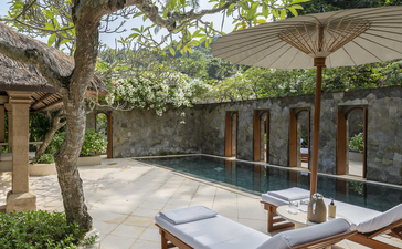 Amankila resort pool suite with lounger beneath a mature tree and modern pavilion.