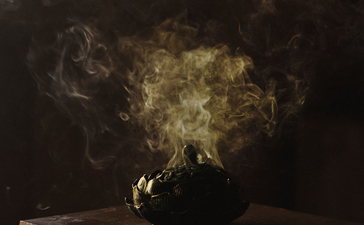 Amankila spa resort: golden steam rising from a dark vessel on a wooden base against a dark background.
