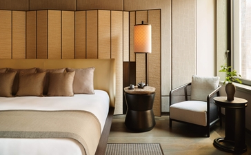 Suite angolare presso Aman New York con letto matrimoniale, testiera in legno e sedute moderne.