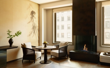 安缦纽约酒店套房内,黑色壁炉旁设有现代座椅,落地窗引入自然光线。