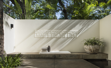 Amansara entrance with cream-coloured wall, geometric shadow, and lush greenery above.