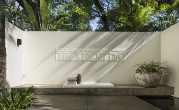 Amansara entrance with cream-coloured wall, geometric shadow, and lush greenery above.