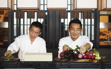 Chef Musashi and Hiraki at the counter of Aman Tokyo's dining venue, preparing cuisine together.