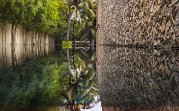 Verdant pathway between stone walls at Amansara, with dappled sunlight filtering through canopy above.