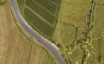 Aerial view of a cyclist riding along a curved road beside a river at Amankila.