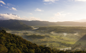 Aerial view of Amankila's verdant valley and distant mountains at sunset.