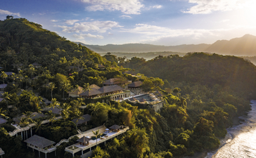 Aerial view of Amankila resort nestled among forested hillsides overlooking a river valley at dusk.