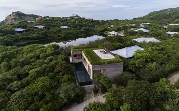 Aerial view of a wellness pool villa at Amanoi, surrounded by forested hills and a lotus lake in Vietnam.