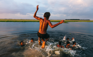 Child in orange shirt running through shallow water at Amansara at sunset.