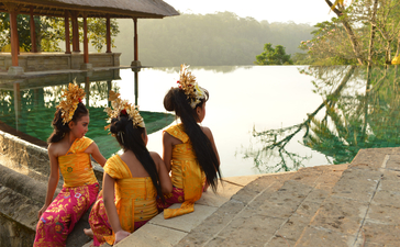 Monks in saffron robes sitting by the riverside at Amandari, with a child in traditional dress nearby.