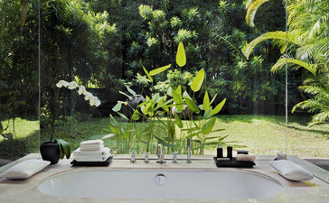 Bathroom at Aman Villas at Nusa Dua with contemporary fixtures and lush tropical greenery visible through open spaces.