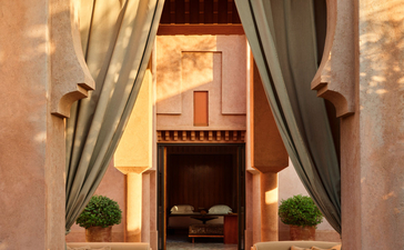 安缦珍纳度假村的Al Hamra套房入口，拱形门框内可见餐饮区，配有石墙和柔和的灯光。