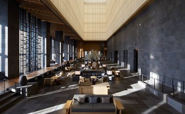 Aman Tokyo's lobby features a serene linear space with warm timber ceiling, dark stone walls, and carefully placed seating areas bathed in natural light.
